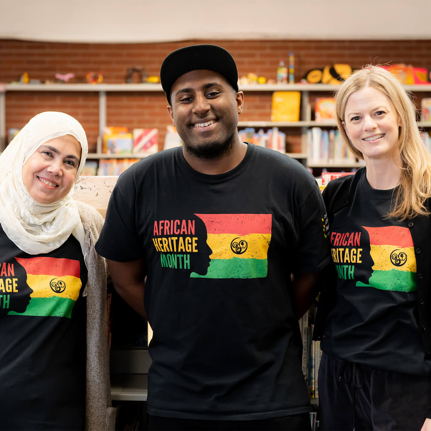 3 staff wearing african heritage month t-shirts smiling to cameara.